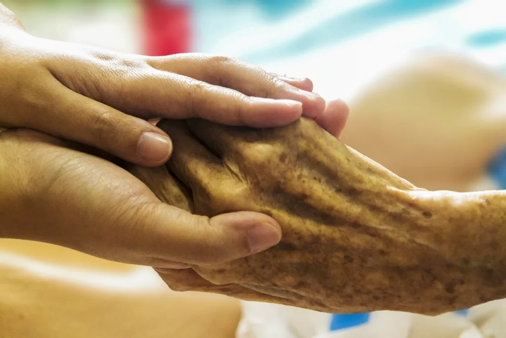A younger person's hands gently holding an older person's hand