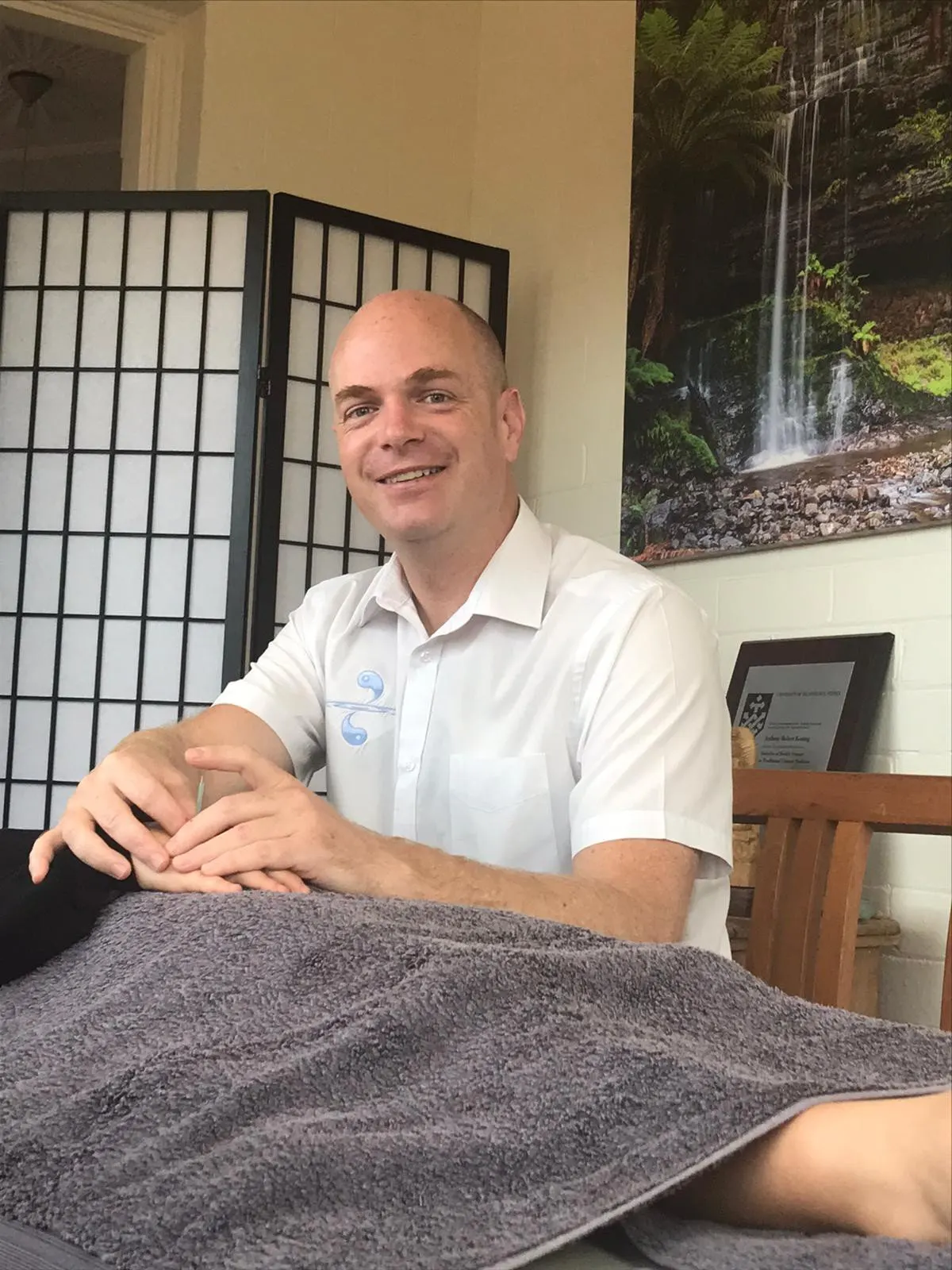 Anthony Keating smiling, sitting beside his treatment table
