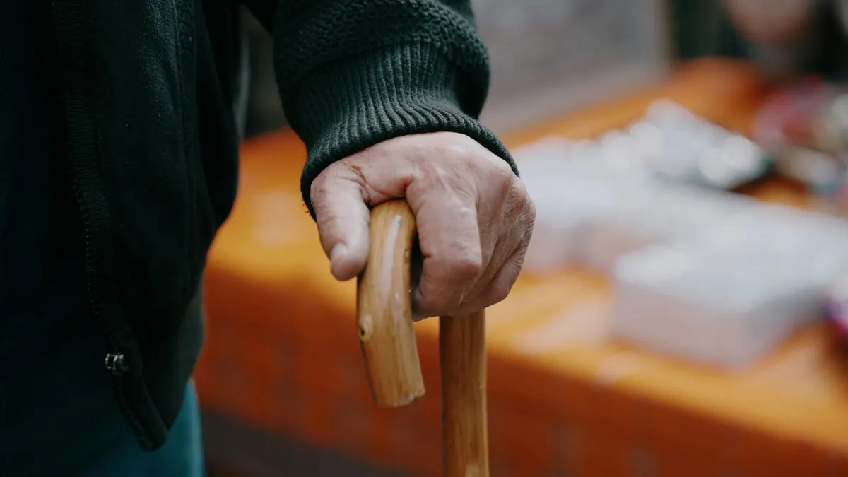 An older person's hand resting on a wooden walking stick